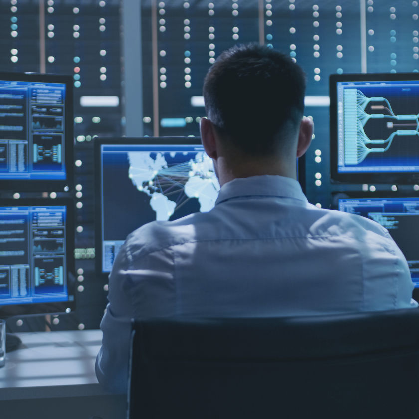 System Security Specialist working in the System Control Center in a room full of screens displaying various information