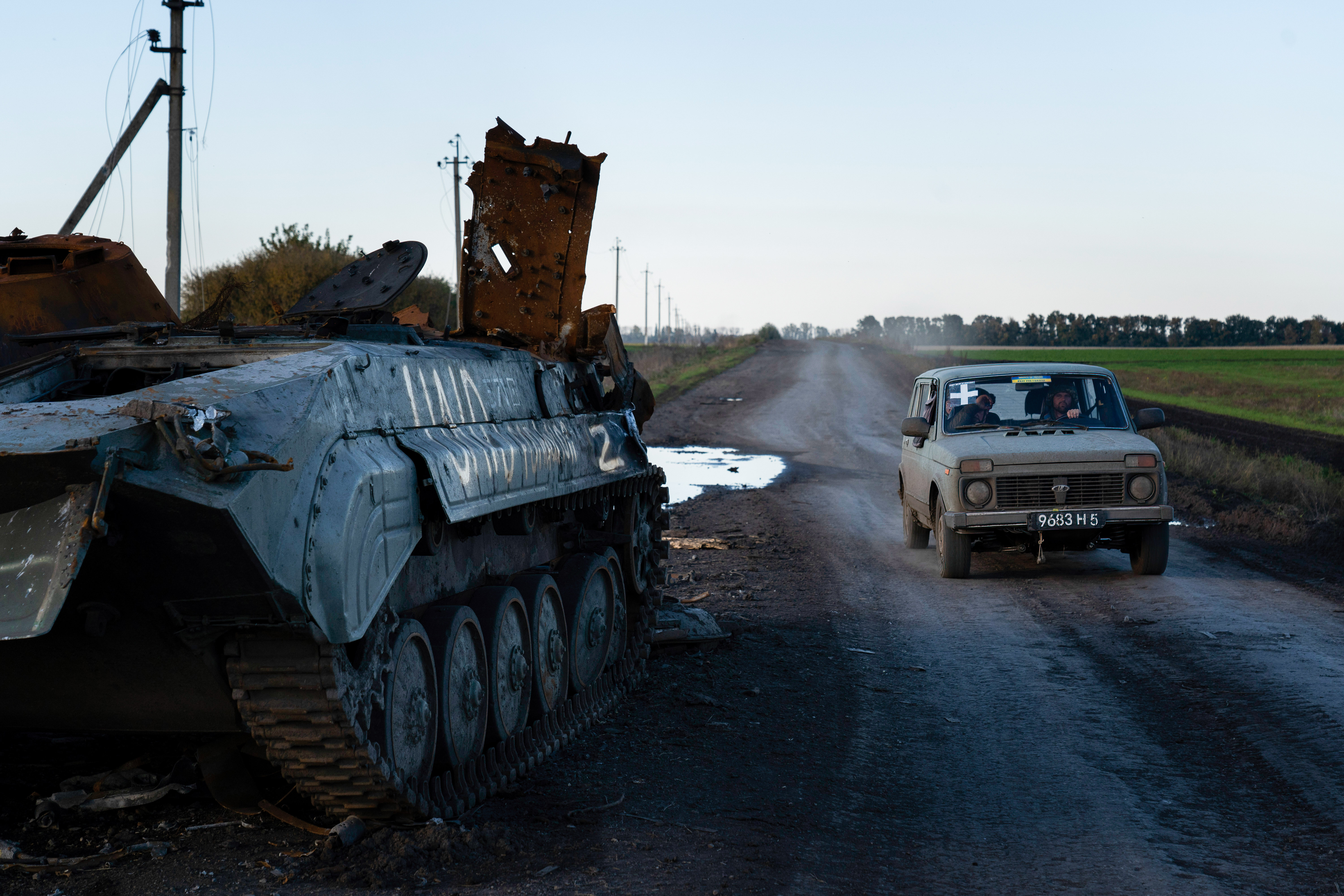 A vehicle with the sign “+”, markings often found on Ukrainian army vehicles, seen driving past a destroyed tank with the sign “Z”, markings often found on Russian military vehicles near the border of Kharkiv and Donetsk region, 2022. 